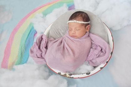 A newborn grant baby swaddled beside a rainbow